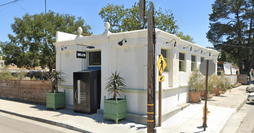 A white building with a sign reading "Bill's," surrounded by greenery and street signs.