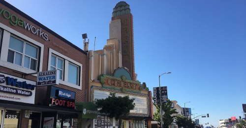 Historic Crest Theater building with colorful signage, surrounded by modern storefronts under a clear blue sky.