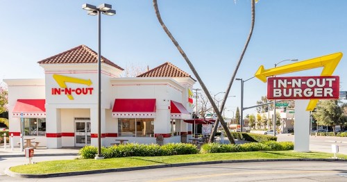 Exterior of an In-N-Out Burger restaurant featuring a red and yellow sign, palm trees, and outdoor seating.