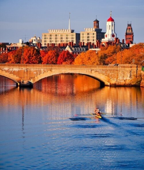 A serene river scene with a bridge, autumn trees, and a rower gliding across the water, set against a city skyline.