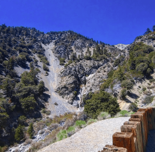 A rocky mountain landscape with a clear blue sky and a wooden barrier in the foreground.