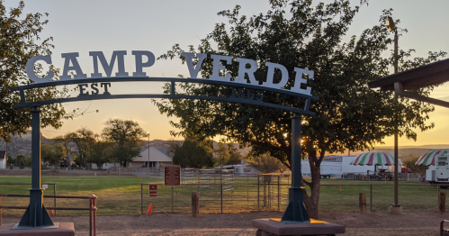 Sign for Camp Verde at sunset, with trees and a grassy area in the background.