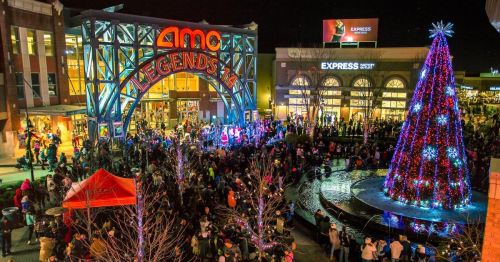 A festive crowd gathers outside the AMC theater, with a brightly lit Christmas tree and decorations in the evening.