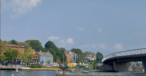 A scenic view of a river with colorful buildings and a modern bridge in the background under a clear blue sky.