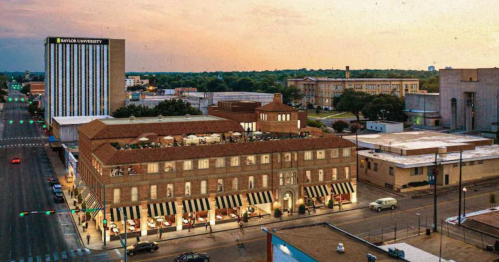 Aerial view of a historic building with outdoor dining, near Baylor University, at sunset with cityscape in the background.