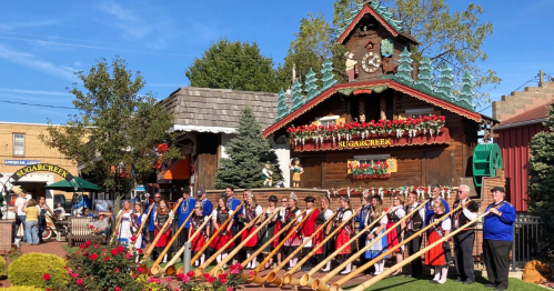 A group of people in traditional attire playing large wooden horns in front of a festive, decorated building.
