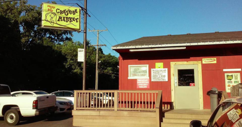 A red building with a sign reading "Creature Market," featuring a wooden deck and parked cars nearby.