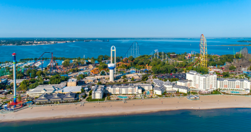 Aerial view of a beachside amusement park with rides, hotels, and a clear blue sky over a calm lake.