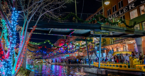 A vibrant night scene of a canal with colorful lights, a bridge, and people enjoying the festive atmosphere.