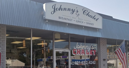 Sign for Johnny's Chalet, a restaurant offering breakfast, lunch, and dinner, with an American flag outside.