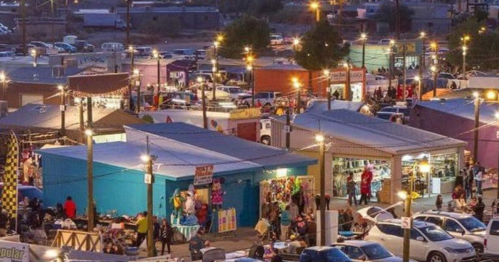A vibrant night market scene with colorful stalls, people shopping, and twinkling lights illuminating the area.
