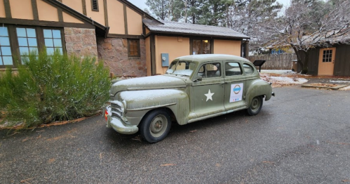 A vintage green car with a star emblem parked on a snowy street near a rustic building.