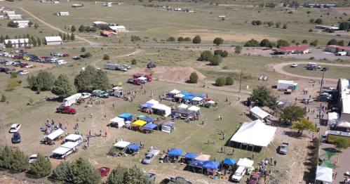 Aerial view of a community event with tents, cars, and people gathered in an open field.