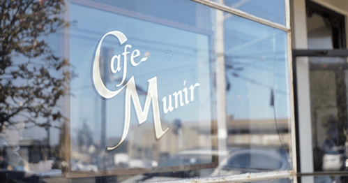 A close-up of a cafe window displaying the name "Cafe Munir" in elegant lettering.
