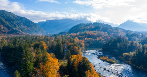 Aerial view of a vibrant autumn landscape with mountains, a river, and colorful trees under a blue sky.