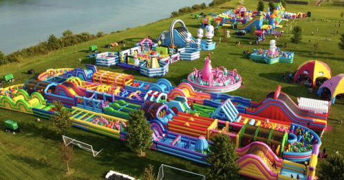 Aerial view of a colorful inflatable amusement park with various slides and obstacle courses set in a green field.