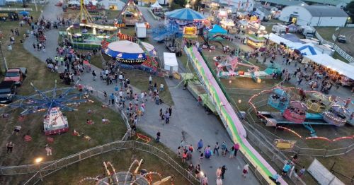 Aerial view of a lively fairground with rides, games, and crowds enjoying the festivities.