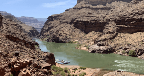 A scenic view of a winding river surrounded by rugged cliffs and desert terrain under a clear blue sky.