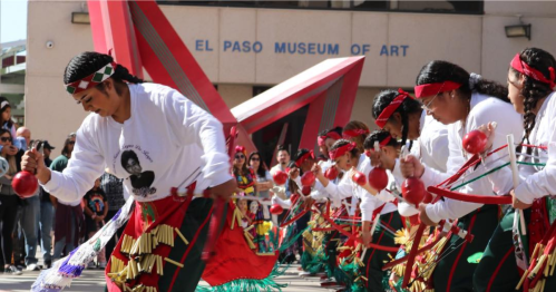 A group of dancers in traditional attire perform with instruments outside the El Paso Museum of Art.
