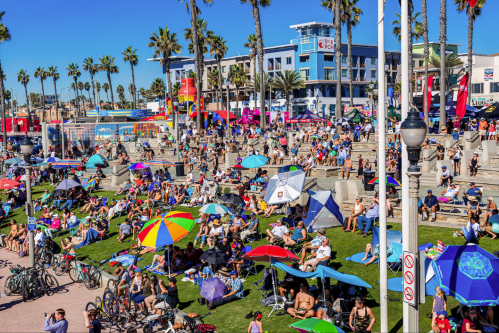 A vibrant beach scene with crowds of people under colorful umbrellas, enjoying the sun and festivities by the ocean.