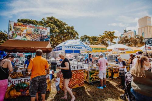 A lively outdoor food market with colorful stalls, people enjoying various food options under sunny skies.