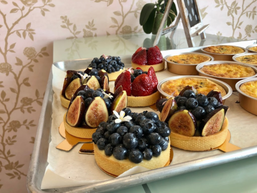 A tray of assorted desserts featuring fruit tarts topped with blueberries, figs, and strawberries, alongside custard cups.