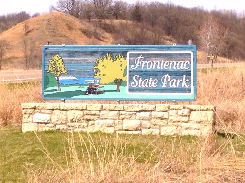Sign for Frontenac State Park featuring trees, water, and a scenic landscape in the background.