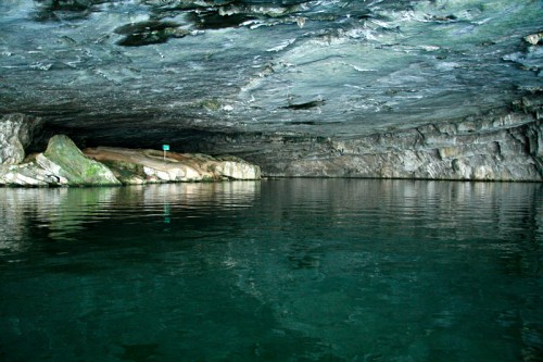 A serene underground cave with smooth rock walls and calm water reflecting the ceiling.