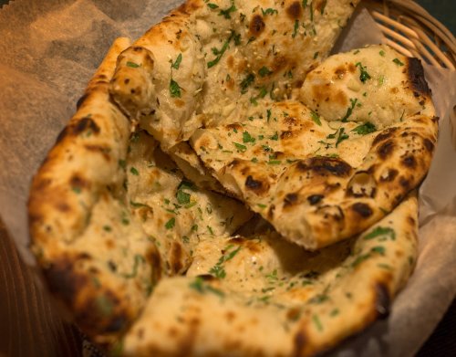 A basket of warm, freshly baked naan bread, garnished with herbs and slightly charred.
