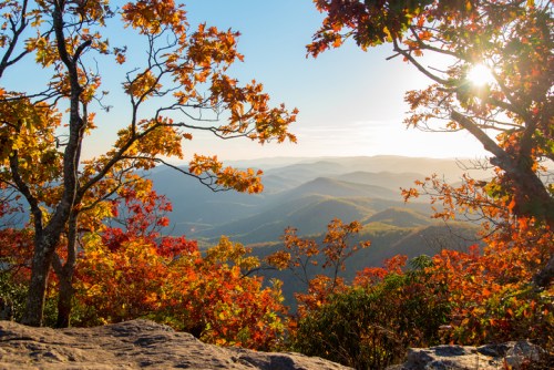 A scenic view of mountains and colorful autumn foliage under a bright sun.