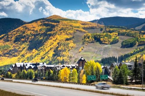 Scenic view of a mountain with vibrant fall foliage and a highway in the foreground.