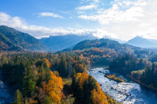 A scenic view of a river winding through autumn-colored trees and mountains under a bright blue sky.