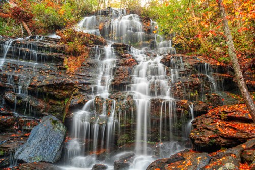 A serene waterfall cascading over rocky terrain, surrounded by vibrant autumn foliage.