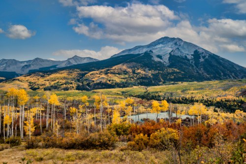 A scenic landscape featuring mountains, colorful autumn foliage, and a serene lake under a partly cloudy sky.