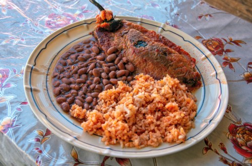A plate of food featuring a fried fish, rice, and black beans on a floral tablecloth.