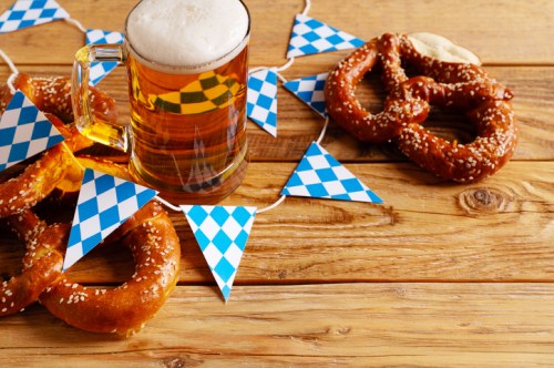 A mug of beer, pretzels, and blue and white bunting on a wooden table, evoking a festive atmosphere.