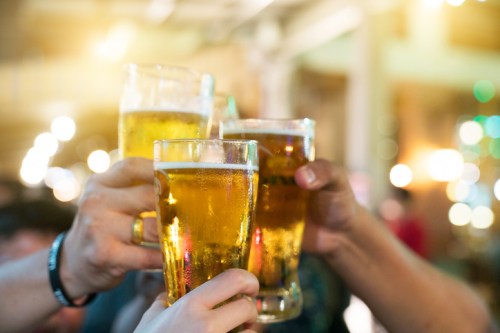 A group of hands toasting with glasses of beer in a lively, blurred background.