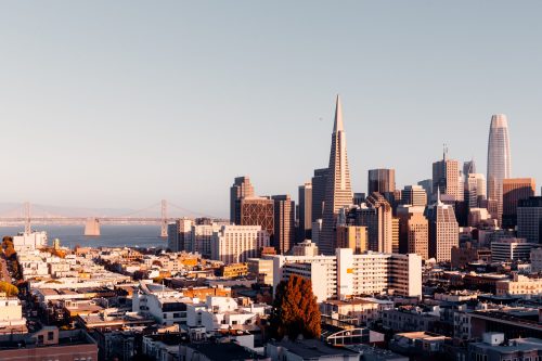 A panoramic view of San Francisco's skyline at sunset, featuring iconic buildings and the Bay Bridge in the background.