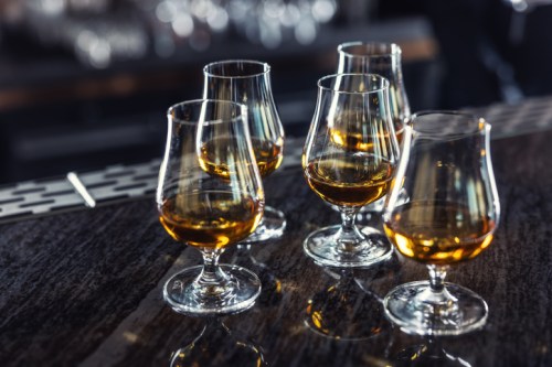 Five glasses of whiskey on a dark bar countertop, reflecting soft light.