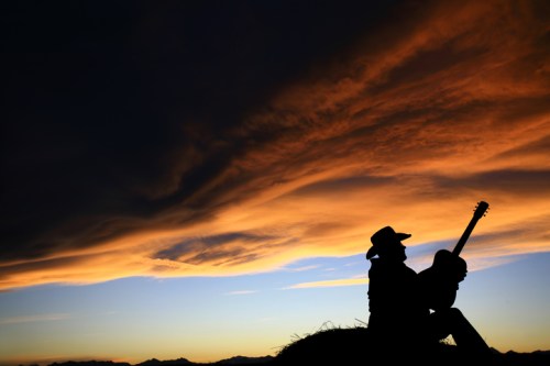 Silhouette of a person with a guitar against a dramatic sunset sky with clouds.