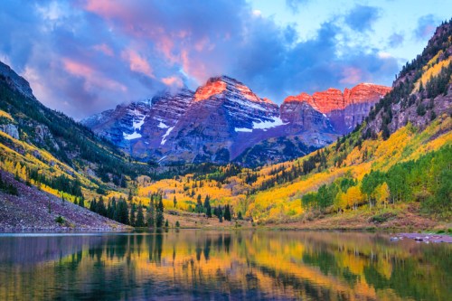Scenic mountain landscape with colorful autumn foliage reflecting in a calm lake under a vibrant sky.