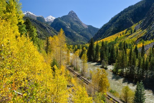 A scenic view of a river winding through mountains, surrounded by vibrant autumn foliage and clear blue skies.