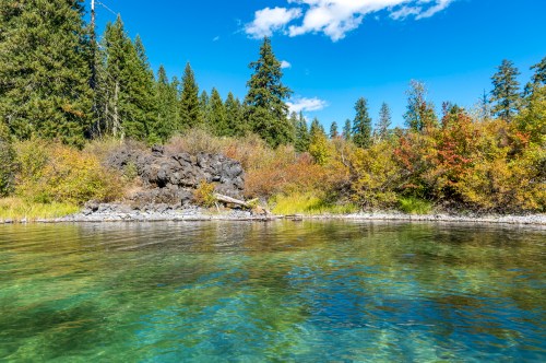 A serene lake surrounded by lush greenery and colorful autumn foliage under a clear blue sky.
