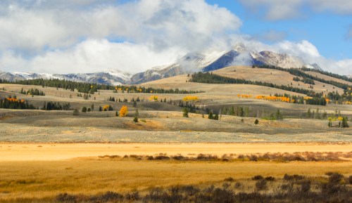 A scenic landscape featuring mountains, rolling hills, and a golden field under a partly cloudy sky.