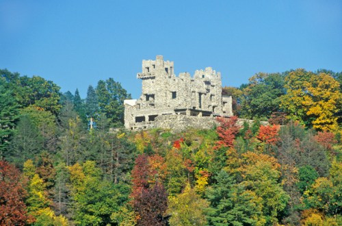 A stone castle ruins atop a hill, surrounded by vibrant autumn foliage in various shades of red, orange, and green.