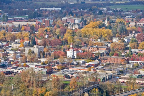 Aerial view of a town surrounded by colorful autumn trees and buildings, with a prominent white building in the center.