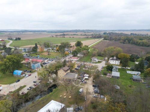 Aerial view of a small rural town with houses, roads, and fields under a cloudy sky.