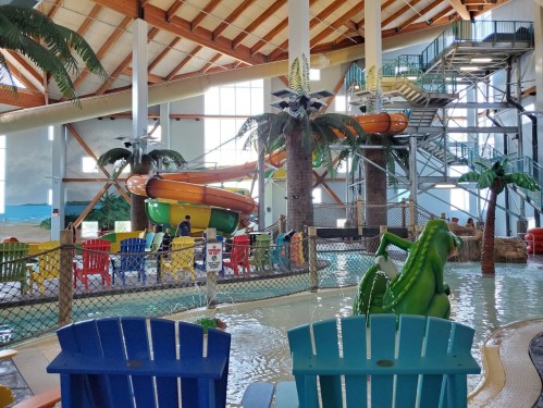 Indoor water park featuring colorful slides, palm trees, and a shallow pool with seating in the foreground.