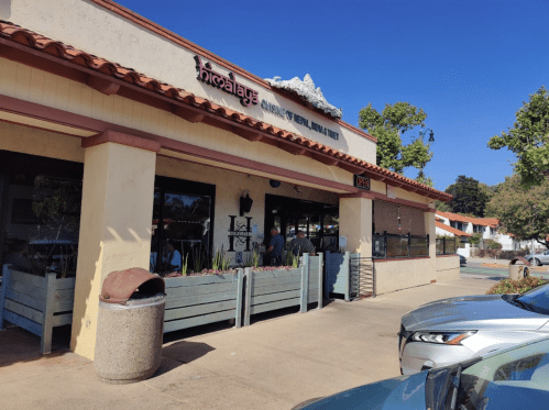 A restaurant with a red-tiled roof and outdoor seating, surrounded by trees and a clear blue sky.