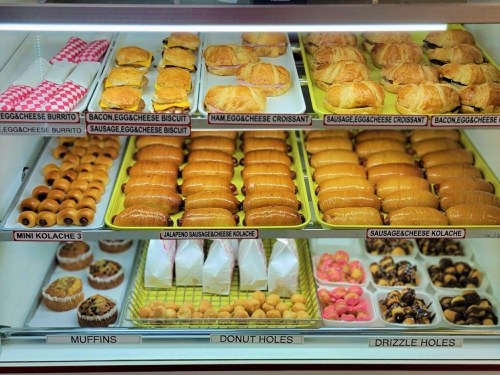 A display case filled with various baked goods, including croissants, kolaches, muffins, and donut holes.